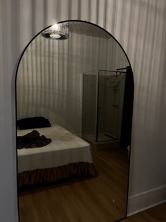 Arched mirror reflecting the bed and glass shower